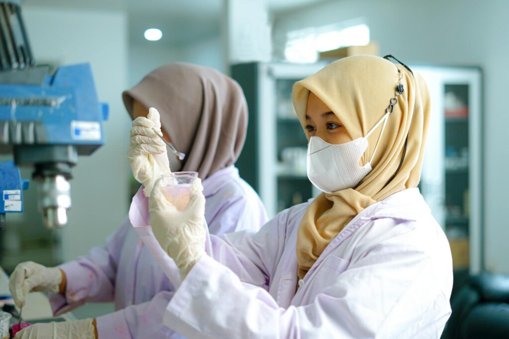 Two Indonesian female researchers conducting experiments in a modern lab, wearing masks and hijabs.